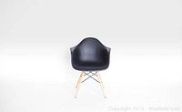 Front view of one black Eames style chair showing molded curved seat, armrests, and wooden legs with metal supports
