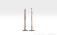 Two tall wooden sculptures on black metal bases, viewed from the side, showing texture and carving details.