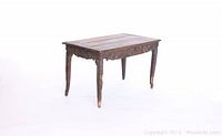 Angled view of antique solid wood table showing carved details on legs and apron, wood grain top with wear.