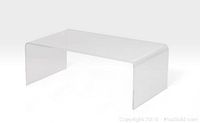 Front angle view of clear Lucite waterfall coffee table showing curved edges and transparent material.