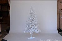 Front view of the full 6.5 foot tall white artificial tree standing on a white metal base, showing dense white faux pine branches.