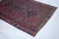 Close-up showing detailed corner of the red vintage rug with patterns and signs of wear.