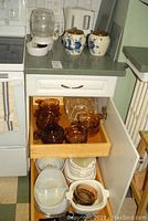 Open kitchen drawer and cabinet displaying amber Corningware Cornflower casserole dishes and white ceramic bowls and dishes.