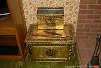 Both brass-colored wood boxes stacked, large bottom and smaller organizer top, showing embossed scenes and floral borders