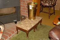 Image showing one wooden stool with floral upholstery and a brass finish umbrella stand placed on it beside a brick fireplace.