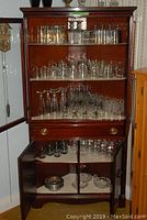 Wooden cabinet with multiple glass types arranged on three shelves and in lower cabinet, showing variety of beer, old fashioned, snifter, champagne, and wine glasses.