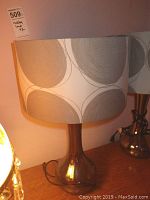 Pair of modern table lamps with brown glass bases and gray circular swirl pattern lampshades sitting on wood surface