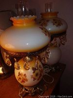 Pair of vintage glass oil lamps with painted floral motifs, crystal prism decorations, metal bases, and clear glass chimneys.