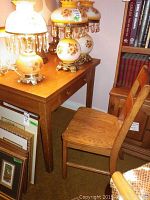 Oak desk and oak chair with lamps on the desk and picture frames nearby