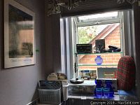 Overview of window sill showing various personal care items, first aid kits, blue glassware, and part of the room with red plaid soft bag.