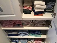 Photo showing four shelves with stacks of assorted towels in varying colors including pinks, blues, and whites