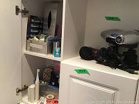 Wide view of cabinet shelf showing hair dryers, black and silver, with cords and attachments.