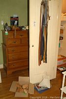 Belts hanging on closet door, a wooden dresser visible in the background with various items on top including a telephone and cleaning supplies.