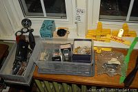 Full overview of lot items arranged on a windowsill showing watches, compasses, pocket knives, chip clips, and various tools