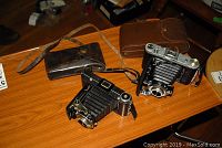 Both folding cameras and their cases displayed on wooden table.