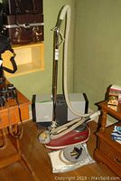 Red TriStar Turbo Brush vacuum cleaner standing upright with hose and handle attached, displayed on a wooden floor near furniture.