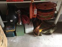 Overall view of lot showing knapsack, metal tackle box, power box, first aid kit and extension cord reels below a shelf.