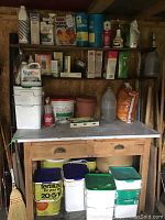 Wide view showing shelf with assorted garden chemicals, fertilizers, containers, plant pots and tools in a backyard shed.