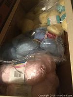 View of yarn skeins in various pastel colors arranged in the first drawer, including pink, blue, and yellow shades. Yarn mostly in plastic bags.