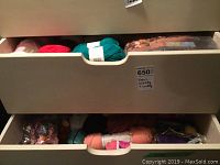 Two open drawers filled with assorted balls and skeins of yarn in multiple colors, with labels visible on some yarns.