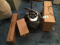 Filter Queen vacuum canister with attached hose, coiled on blue carpet alongside boxes
