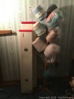 Full view of wooden spool tree holding multiple yarn spools and the tall beige knitting machine case with red top beside it.