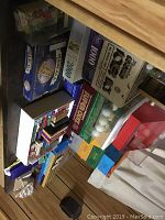 Overview photo showing boxed board games including Trivial Pursuit, 1200-piece puzzle, Super Quiz, and some unknown games stacked.
