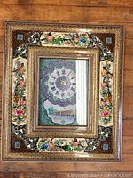 Full view of the decorative wall clock frame showing colorful floral and bird designs surrounding the clock face and scenic illustration