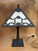 Full view of antique slag glass table lamp showing triangular shade with ornate metal frame and cream-colored glass panels
