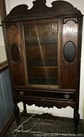 Front view of the vintage china cabinet showing glass panel door, side wooden insets, and drawer at bottom.