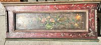 Top front panel of the wooden trunk showing hand painted floral artwork with a mostly red border.