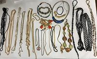 Photo showing multiple necklaces and bracelets arranged flat, displaying variety of materials and styles from chain to beaded pieces.
