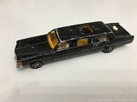 Black Majorette limousine toy car showing side view with visible wear on roof and body and yellow-orange interior visible through windows.