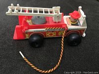 Front and side view of the red and white vintage Fisher Price Toy Fire Engine 720 with a pull string and figurine firefighter.