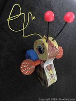 Front angle view showing the yellow wooden bee face with large eyes, red antenna tips, orange wings, blue wheels, and yellow pulling string.