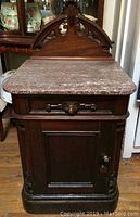 Front view of antique solid wood cabinet with stone top, showing single door and drawer.