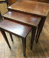 Three mahogany nesting tables stacked showing tops and tapered legs with casters.