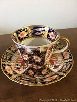 Front angled view of demitasse cup placed on matching saucer, showing intricate Imari pattern colors and designs.