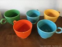 Five vintage ceramic mugs in different colors arranged on a surface, showing overall set.
