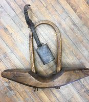 Full view of the antique wood cow yoke with attached metal cow bell on leather strap laid on the wooden floor.