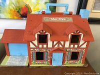 Front view of vintage Fisher Price plastic play house with red roof, blue door and handle on top, labeled Fisher Price 952