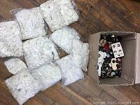 Several clear plastic bags filled with numerous white buttons laid on wooden floor.