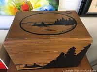 Front view of the pine wood tackle box showing the painted fishing scene artwork on the lid illustrating a fisherman in a boat with a lake and trees, signed Lee Rogers.