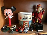 Full lot showing Mickey Mouse head on stand, View-Master Gift Pak, tin toy figure, and seven toy cars.