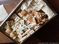 Open wooden box showing Mahjong tiles and some wrapped paper inside.