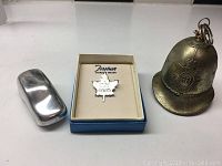 Three mini metal pieces displayed: a silver colored mini car, a sterling silver maple leaf pin in a box, and a small metal bell.