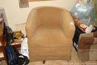 Front view of tan fabric upholstered swivel tub chair showing cushioned seat, tub arms and visible wear on fabric.