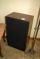 Left speaker angled with wood veneer finish and black grill visible. Shows damaged woofer area covered by grill.