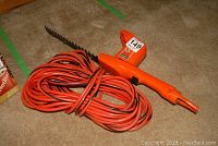 Full view of the hedge trimmer showing orange body, blade, and cord coiled around