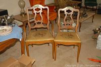Four wood dining chairs with carved backs and yellow needlepoint fabric seats with floral designs arranged near a dining table and other furniture.